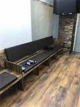 Ein Wartebereich mit hölzernen Sitzbänken und modernem Bodenbelag in einem Friseursalon.