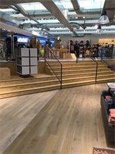 Eine Holztreppe mit Metallgeländer führt zu einem höher gelegenen Bereich in einem hellen Laden.