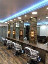 Friseurstühle vor großen Spiegeln mit Holzrahmen und blauer Deckenbeleuchtung in einem Salon.