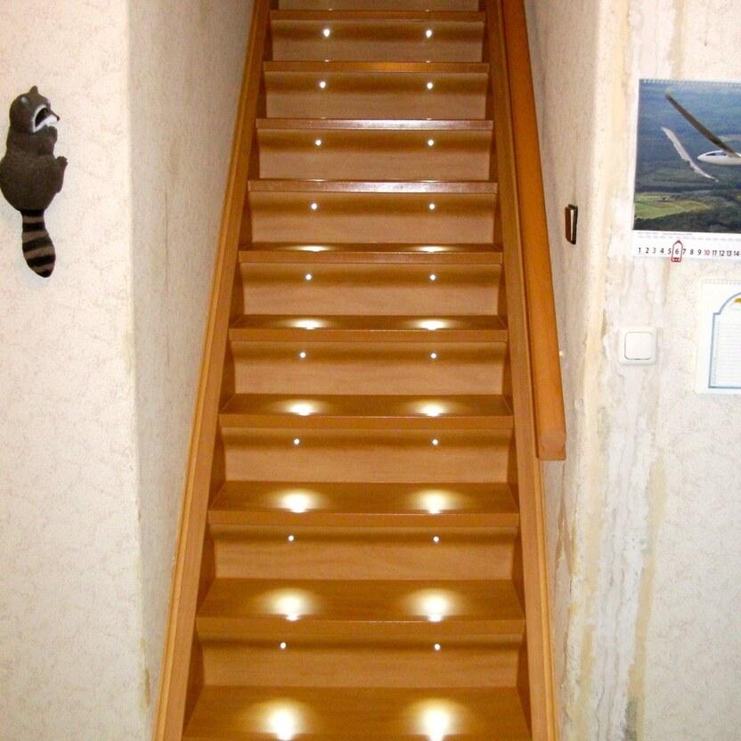 Maßgefertigte Holztreppe mit LED-Stufenbeleuchtung für bessere Sicht und modernes Design in einem Wohnhaus.