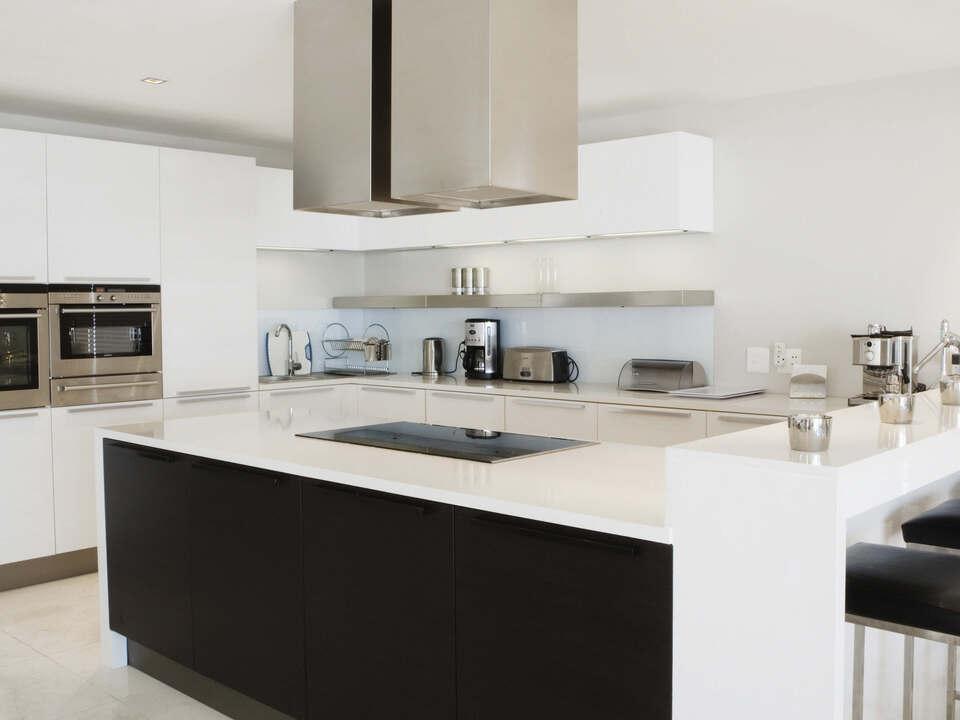 Stilvolle K&uuml;che nach Ma&szlig; in Schwarz-Wei&szlig;-Design mit gro&szlig;z&uuml;giger Kochinsel, Edelstahlger&auml;ten und eleganter Beleuchtung.