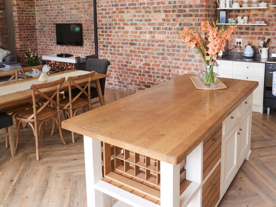 Stilvolle Wohnk&uuml;che mit rustikaler Backsteinwand, gro&szlig;er Holzkochinsel und gem&uuml;tlichem Essbereich f&uuml;r ein modernes Landhausambiente.