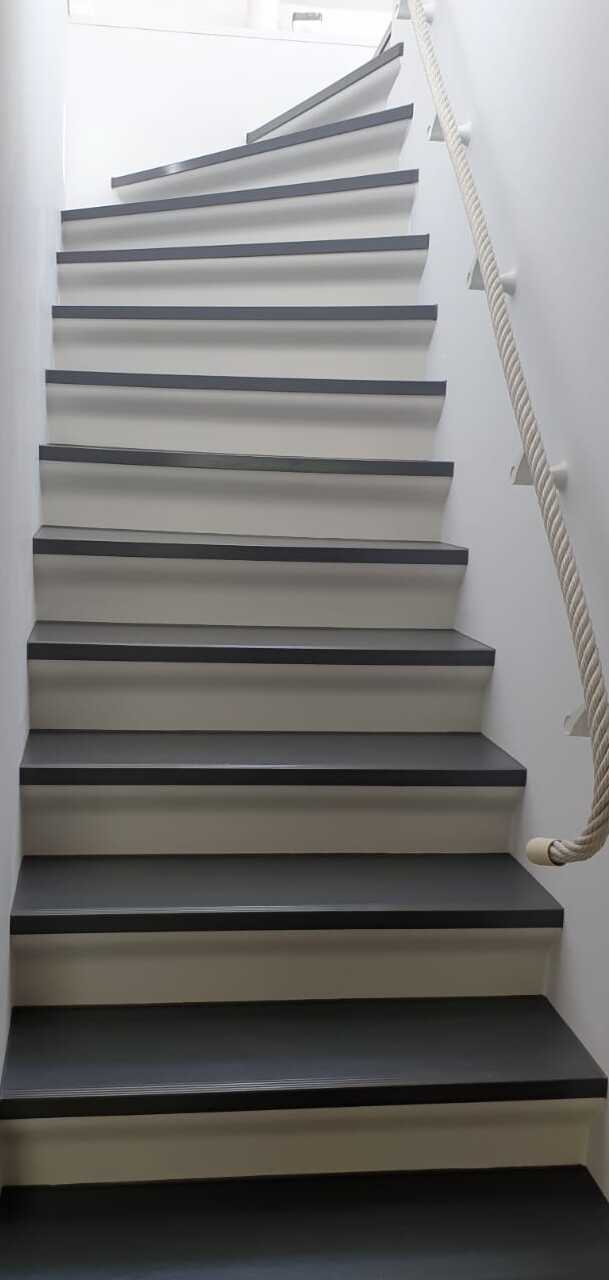 Helle moderne Holztreppe mit grauen Stufen und weißem Geländer in einem minimalistischen Treppenhaus.