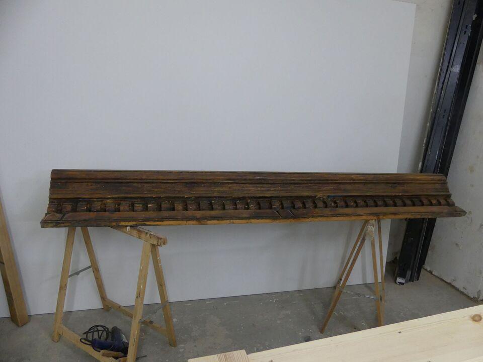 Antikes Holzgesims mit dunkler Patina liegt zur Restaurierung auf zwei Böcken in einer Werkstatt.