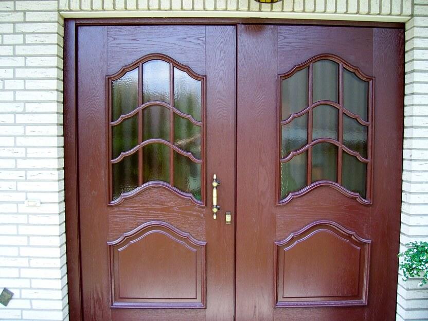 Haustür mit Glas Berlin Doppelflügelige braune Haustür aus Holz mit geschwungenen Glasfeldern und Messinggriff in einer hellen Ziegelwand.