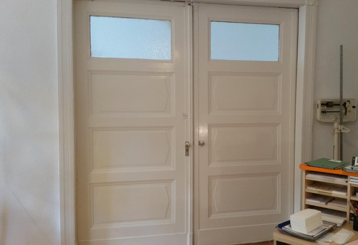 Doppelflügeltür mit Glasfenstern und klassischem Design Alte Doppelflügeltür in Weiß mit eingelassenen Glasfenstern und klassischen Verzierungen, passend für historische Innenräume.